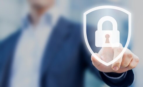 Person im Hintergrund zeigt mit Finger auf ein digitales Symbol für Cybersecurity, ein Schild mit Vorhängeschloss in der Mitte